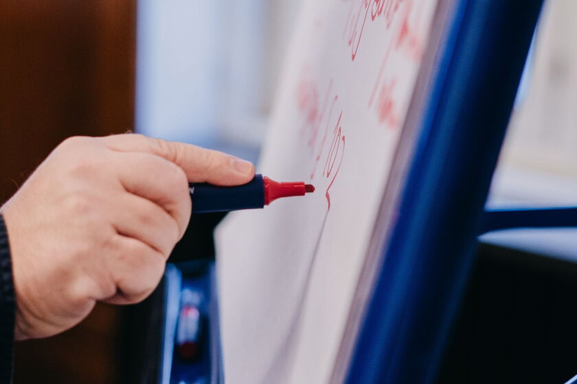 Nahaufnahme: Hand hält roten Marker und schreibt auf ein Plakat.