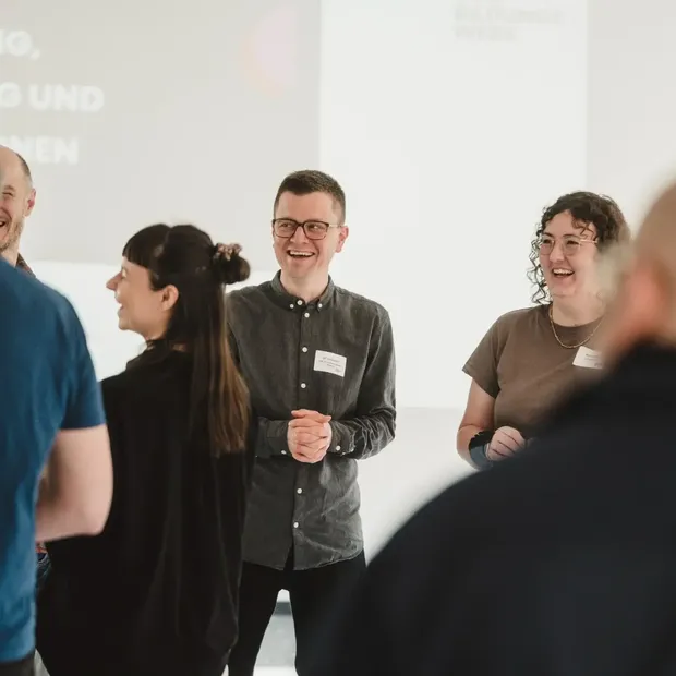 Seminargruppe im Gespräch vor einer Leinwand, mehrere Personen lachen.