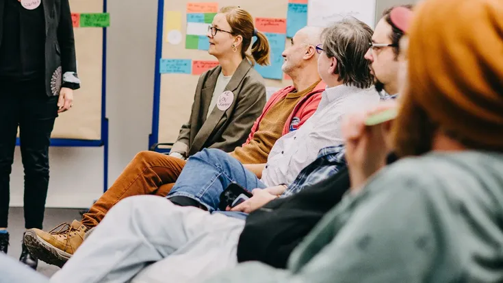 Teilnehmende sitzen in einer Seminargruppe und hören einer moderierten Diskussion zu