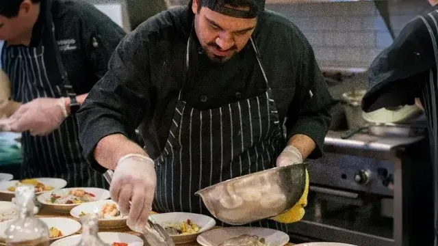 Ein Koch richtet in der Küche Teller mit Fisch und Gemüse an.