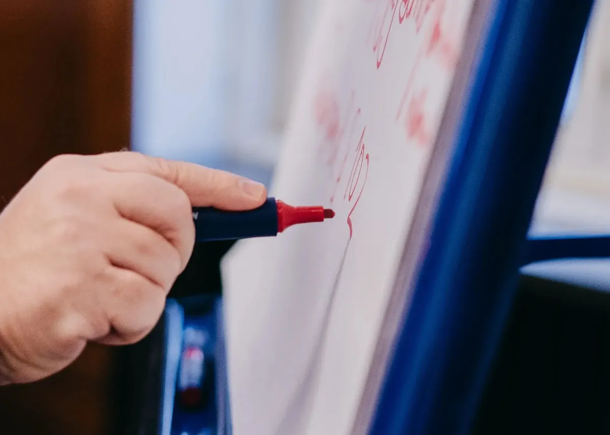 Hand schreibt mit rotem Marker auf ein Flipchart oder Whiteboard