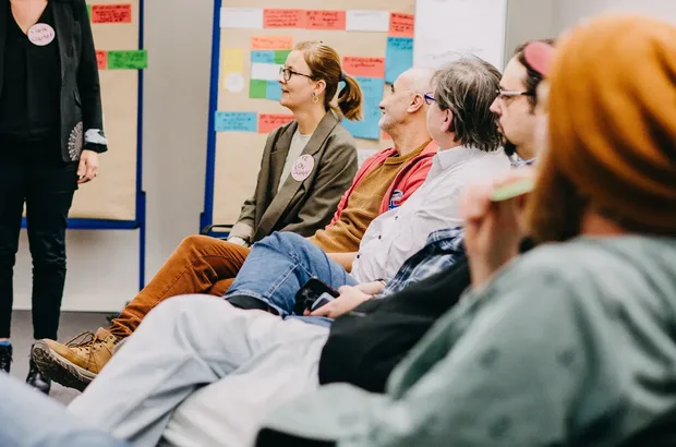 Teilnehmende sitzen in einer Seminargruppe und hören einer moderierten Diskussion zu