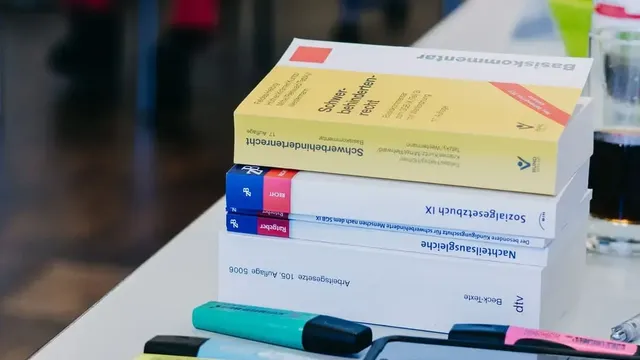 Stapel von Fachbüchern zu Arbeitsrecht und Sozialgesetzgebung auf einem Tisch, daneben mehrere bunte Textmarker.