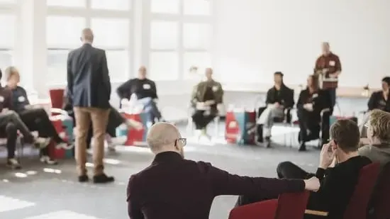 Eine größere Gruppe sitzt in einem hellen Seminarraum in einem Stuhlkreis; im Vordergrund ist eine Person auf einem roten Stuhl zu sehen, während im Hintergrund weitere Teilnehmende sowie bunte DGB-Papphocker mit „#Tarifwende" zu erkennen sind.