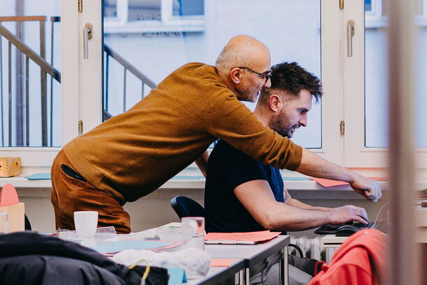 Person zeigt einer anderen Person etwas auf einem Laptop in einem Seminarraum.