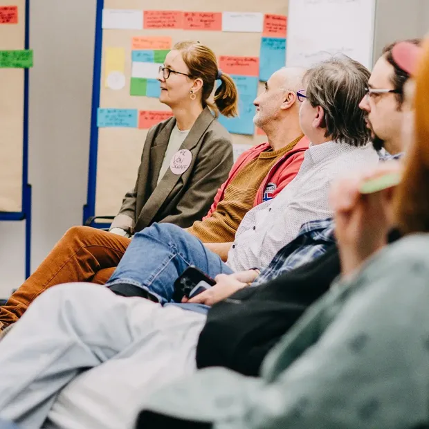 Teilnehmende sitzen in einer Seminargruppe und hören einer moderierten Diskussion zu