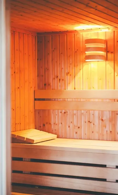 Saunaraum mit Holzbänken und warmer Beleuchtung, angrenzend ein Ruhebereich mit Liegen