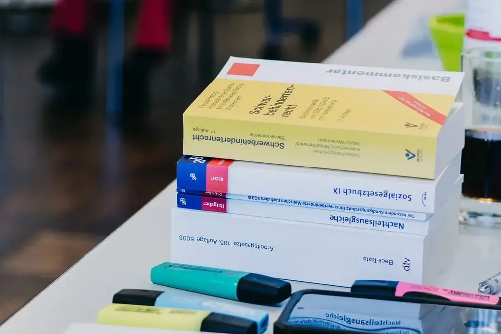 Stapel von Fachbüchern zu Arbeitsrecht und Sozialgesetzgebung auf einem Tisch, daneben mehrere bunte Textmarker.