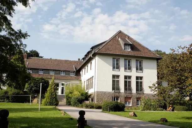 Seminarhaus mit großem Garten und Zufahrtsweg an einem sonnigen Tag.