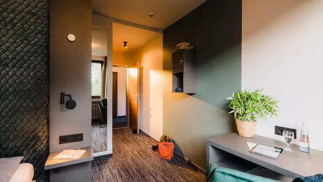 Modernes Hotelzimmer mit Bett, Schreibtisch, Spiegel, Regal und Blick in den Flur