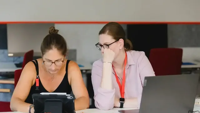 Zwei Personen arbeiten gemeinsam an einem Tisch mit Tablet und Laptop, Schriftzug „DGB Bildungswerk" auf dem Tablet sichtbar.