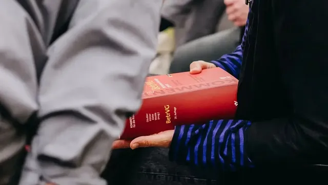 Nahaufnahme einer Person, die ein dickes rotes Fachbuch mit dem Titel „Kommentar BetrVG" hält.