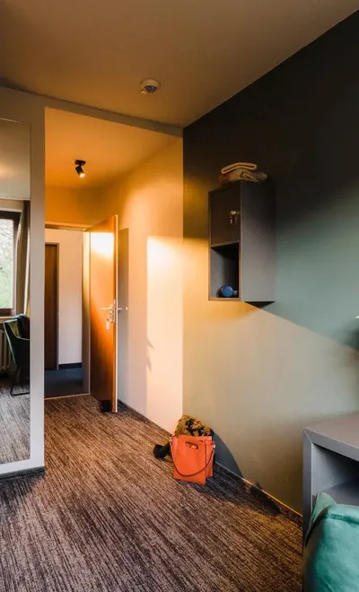 Modernes Hotelzimmer mit Bett, Schreibtisch, Spiegel, Regal und Blick in den Flur