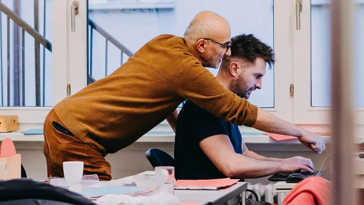 Zwei Teilnehmende arbeiten gemeinsam am Computer, eine Person erklärt etwas und zeigt auf den Bildschirm