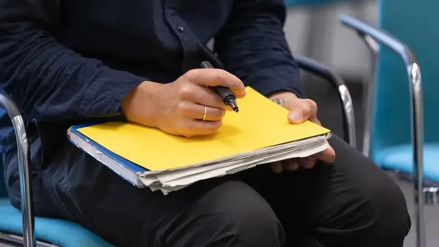 Nahaufnahme einer Person, die auf einem gelben Ordner schreibt, Ordner liegt auf dem Schoß.