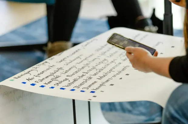 Person fotografiert ein handgeschriebenes Plakat mit Stichpunkten in einem Workshop.