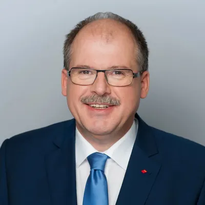 Stefan Körzell im Anzug vor unscharfem Hintergrund, in die Kamera blickend.