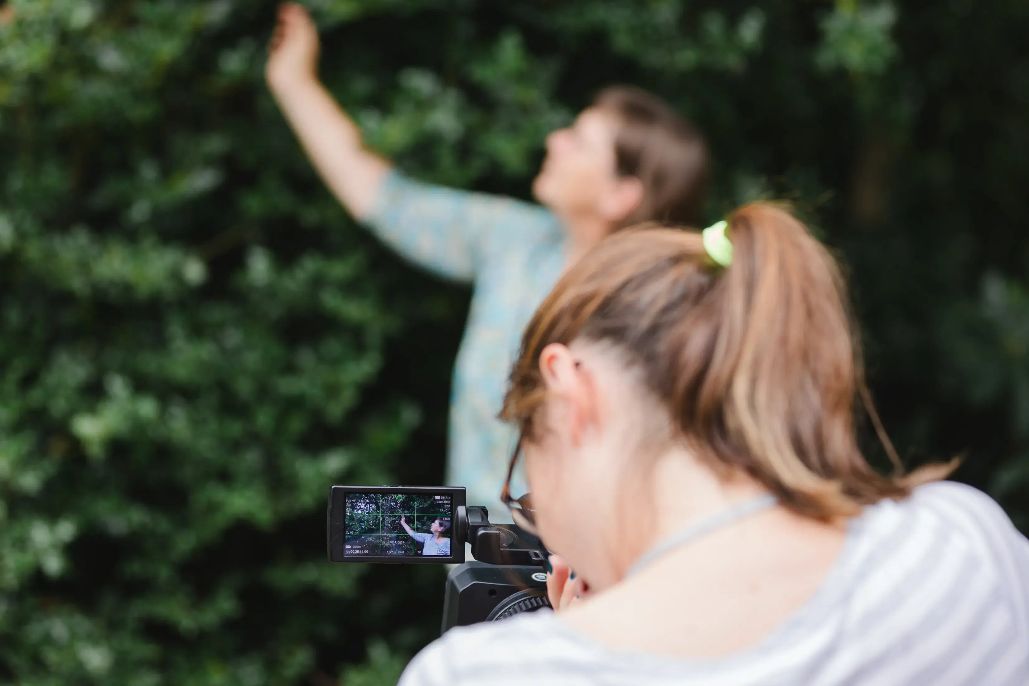Frau von Hinten die eine Kamera in der Hand hält und eine andere Person filmt