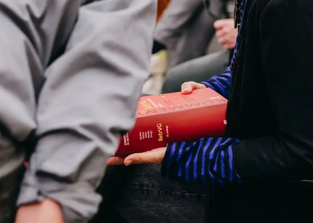 Nahaufnahme einer Person, die ein dickes rotes Fachbuch mit dem Titel „Kommentar BetrVG“ hält.