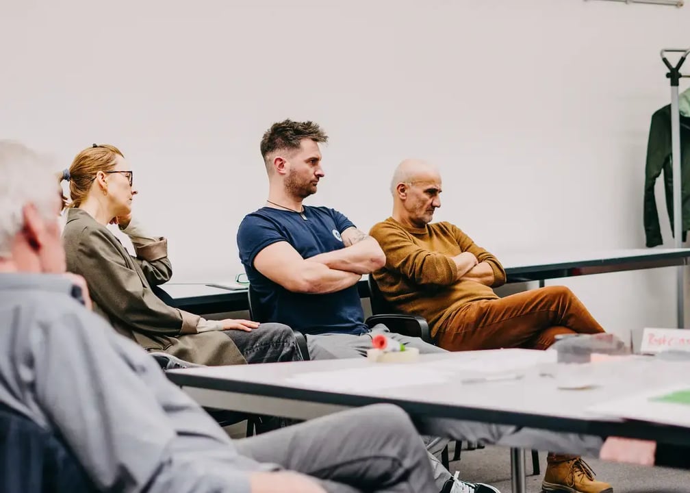 Mehrere Personen sitzen in einem Seminarraum an einem Tisch, auf dem Moderationsmaterialien liegen.