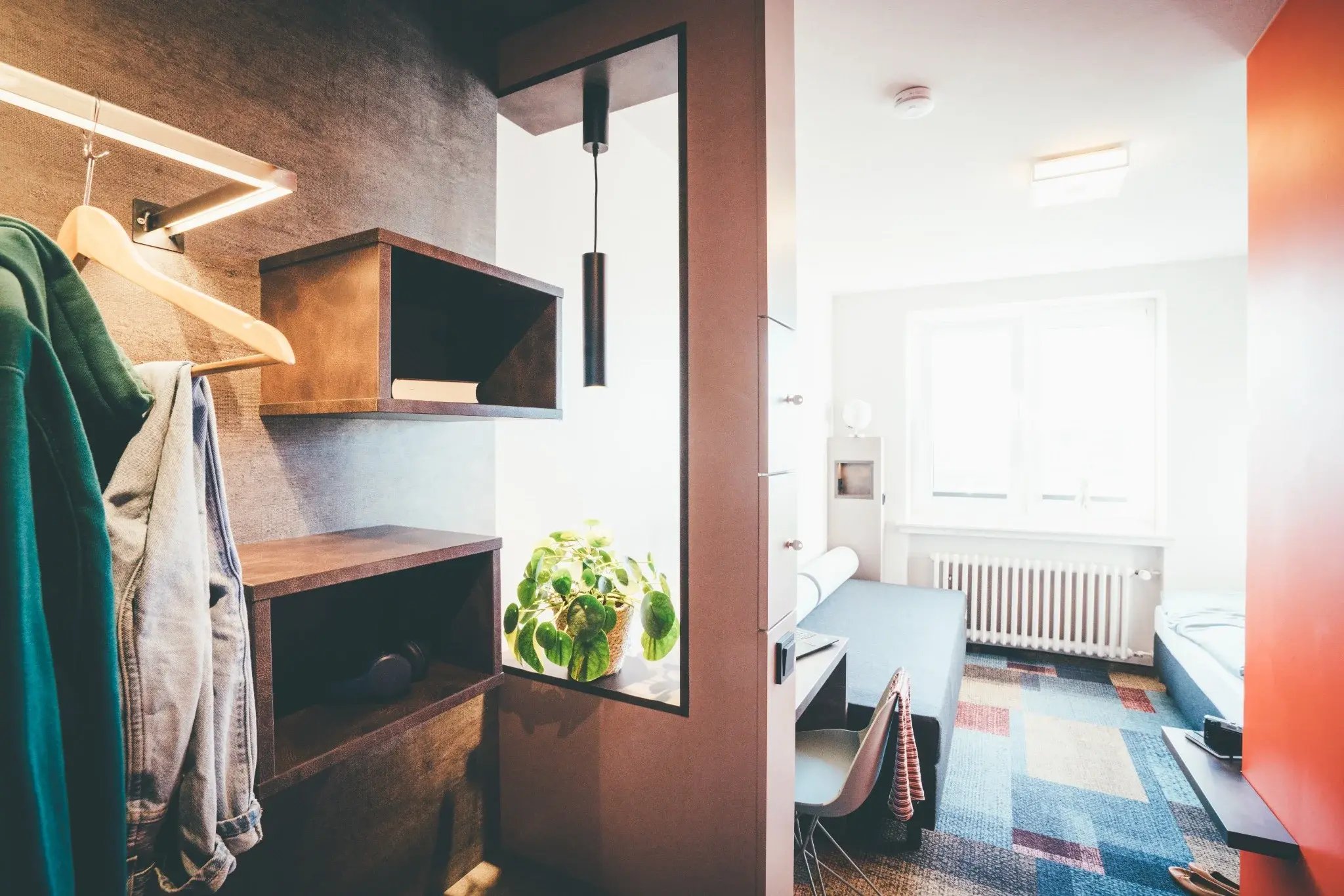 Modernes Hotelzimmer mit offenem Kleiderschrank, Schreibtisch und Bett im Hintergrund.