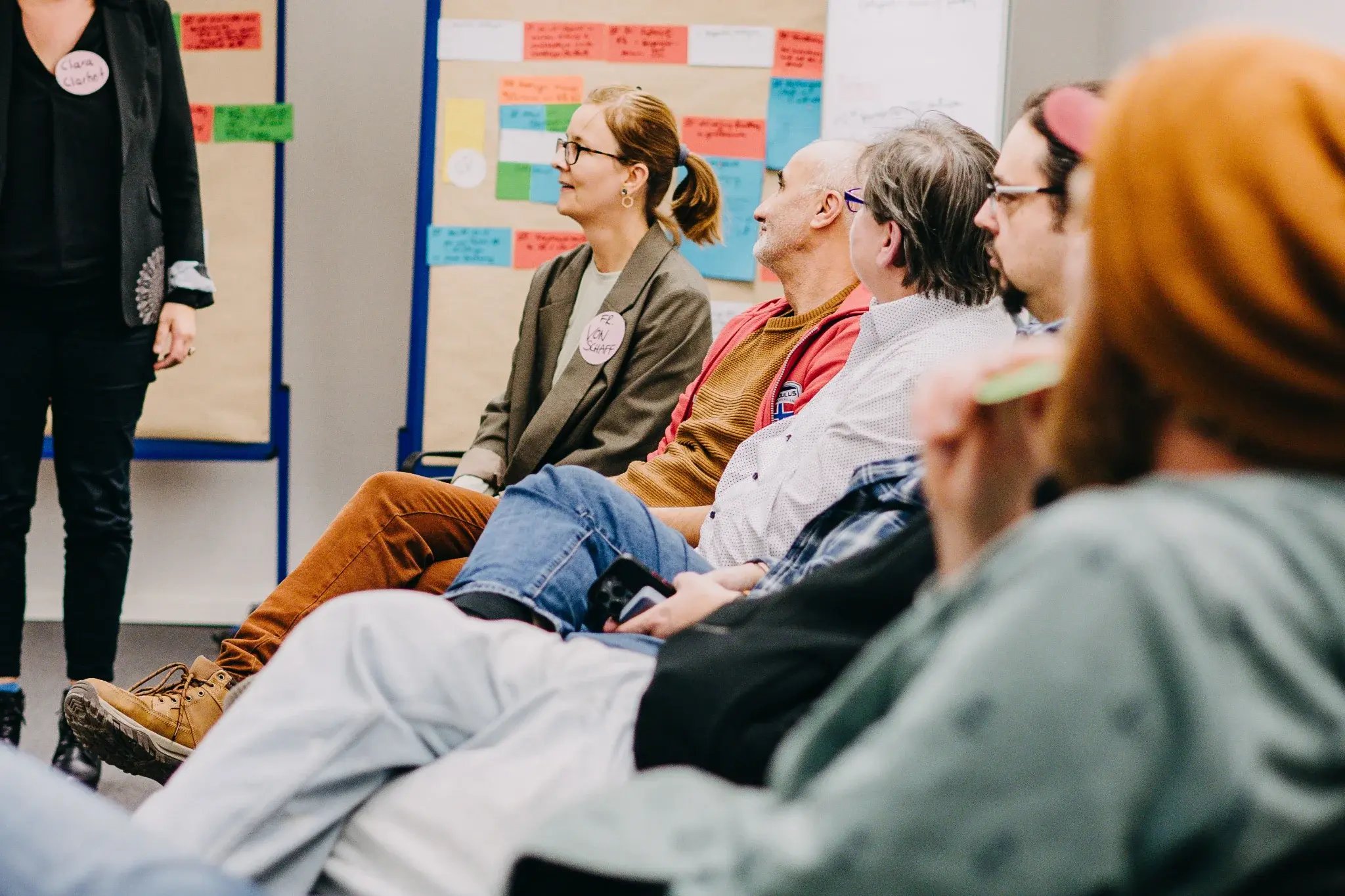 Teilnehmende sitzen in einer Seminargruppe und hören einer moderierten Diskussion zu