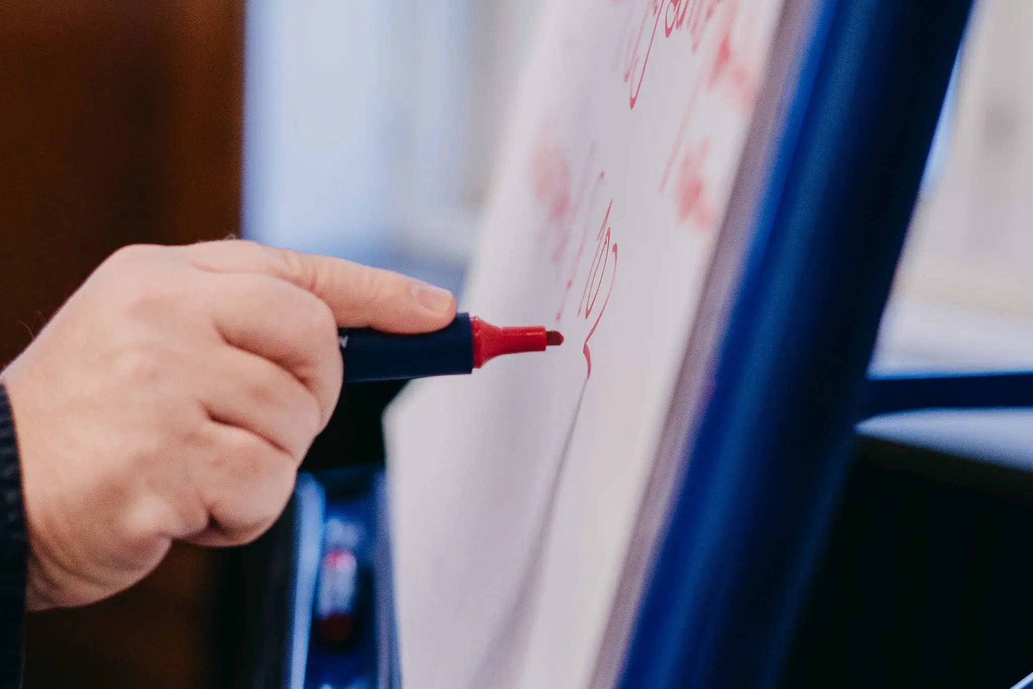 Hand schreibt mit rotem Marker auf ein Flipchart oder Whiteboard