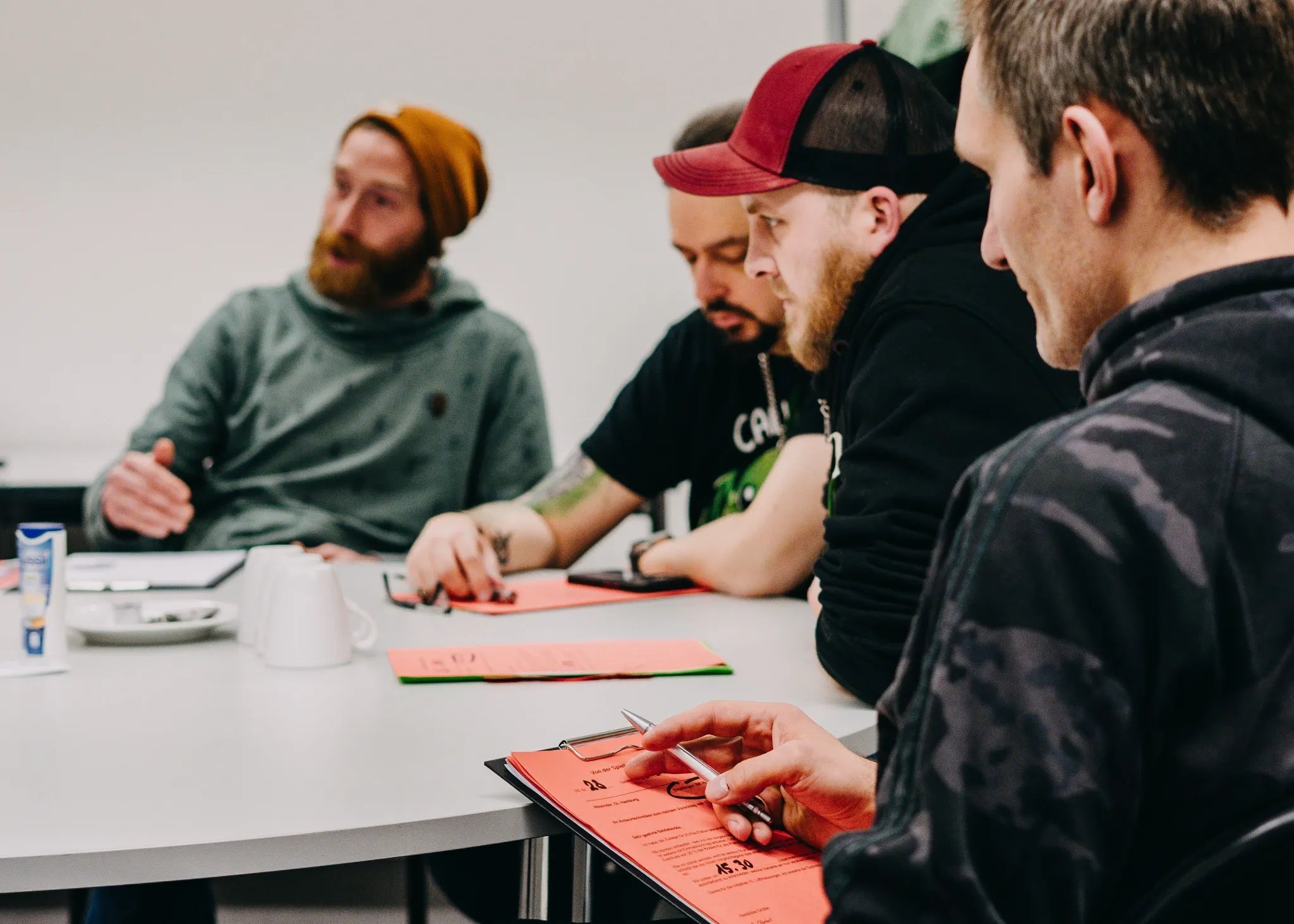 Personen sitzen mit einem Klemmbrett an einem Tisch und reden.