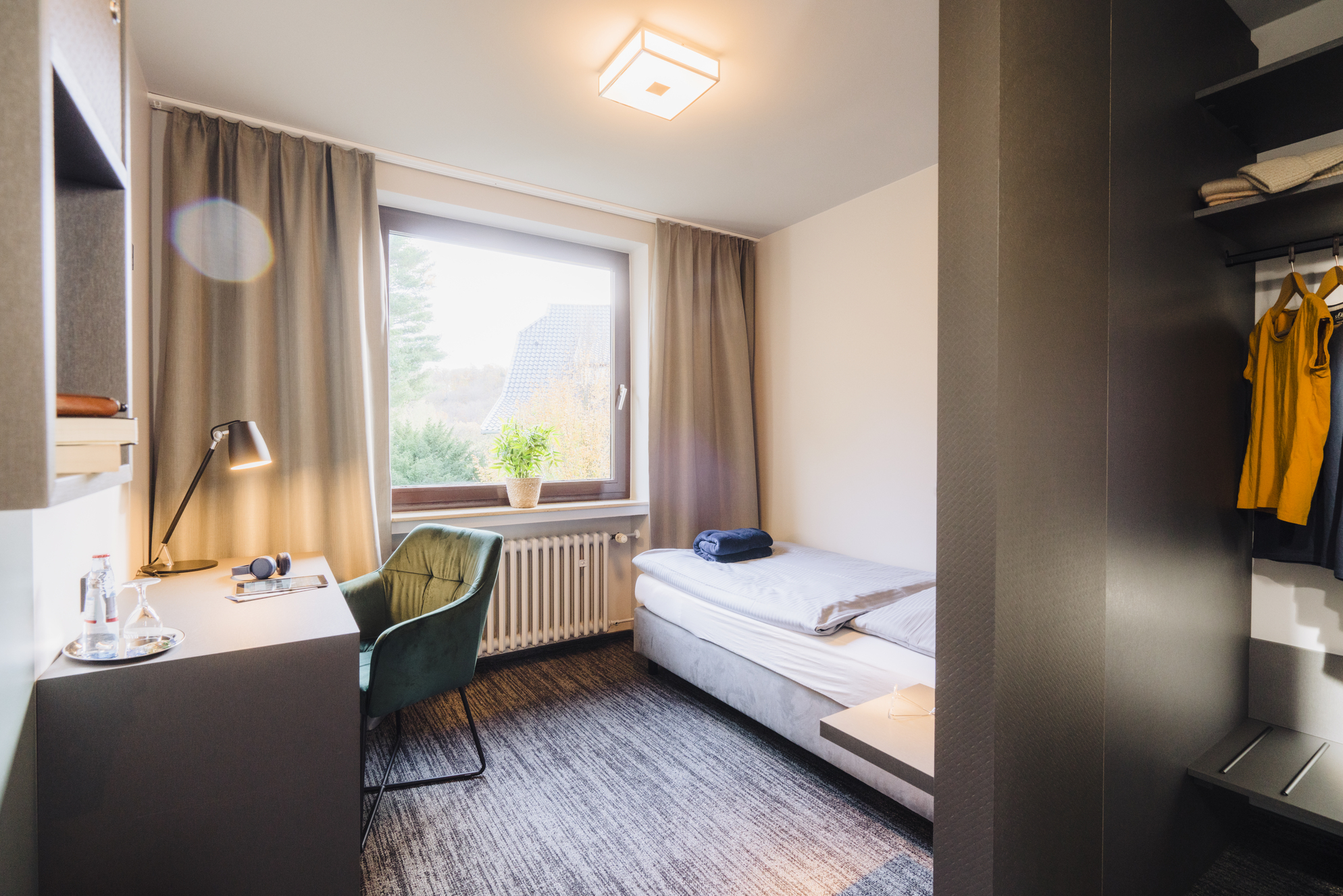 Zimmer im DGB Tagungszentrum Hattingen, ausgestattet mit einem Bett, einem Schreibtisch und einem Kleiderschrank.