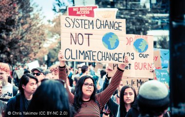 Aktivist_innen halten Schilder auf Protest hoch: System Change Not Climate Change